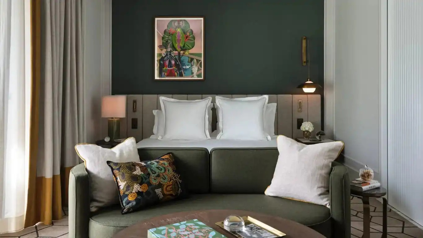 Green loveseat in front of white linen covered bed and green walls